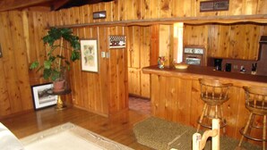A wooden interior with a bar area, wooden chairs, a potted plant, and a framed picture on the wall. - Kern Riverfront Lodge (Kernville)
