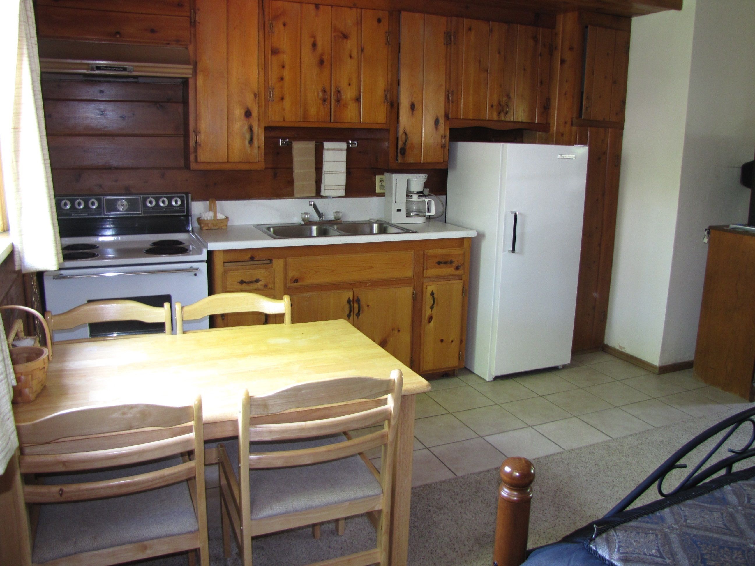 Una cocina compacta con gabinetes de madera, un refrigerador blanco, una estufa y una mesa de comedor con sillas.