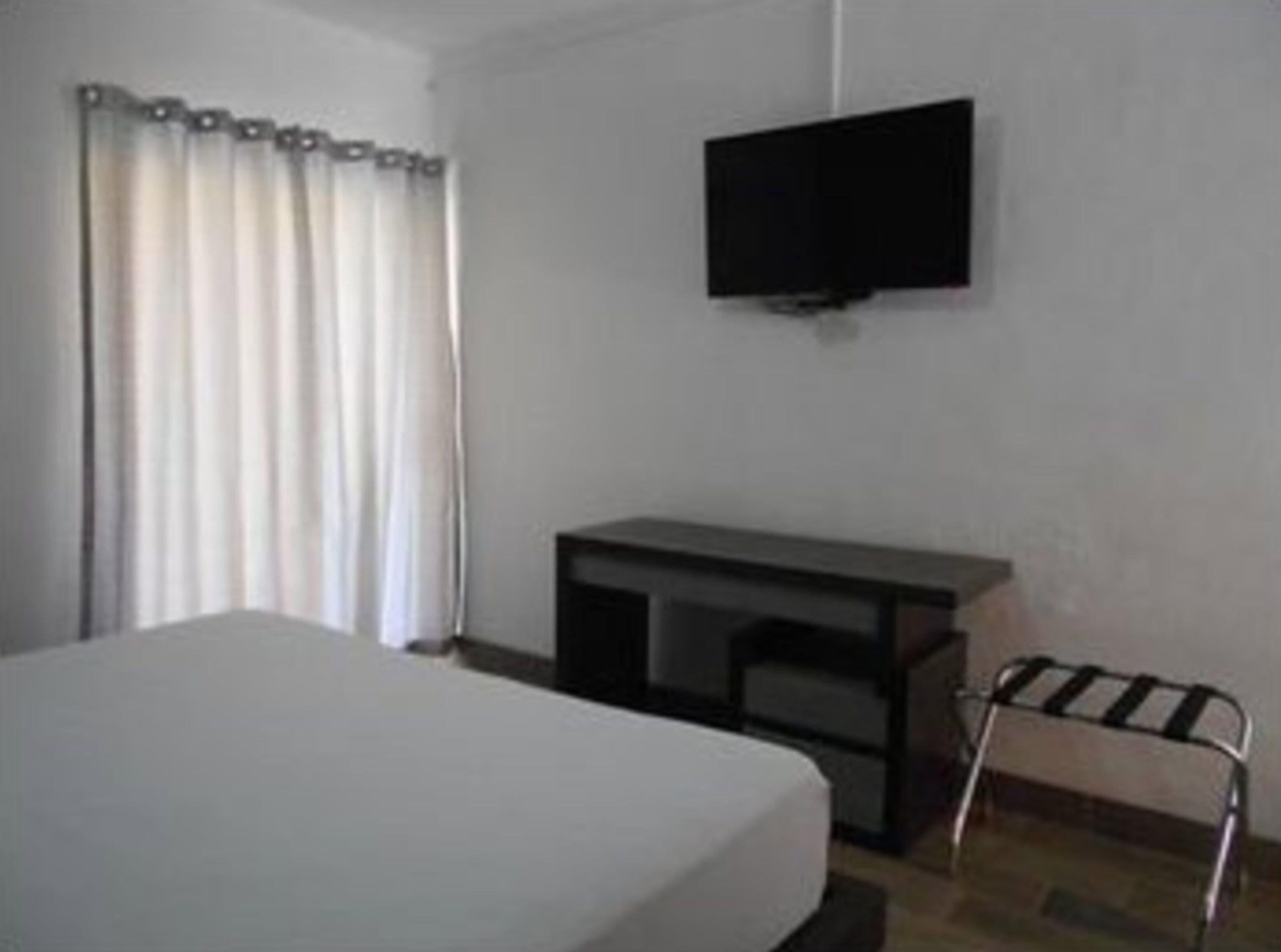 A hotel room with a bed, a desk, a chair, and a TV mounted on the wall.