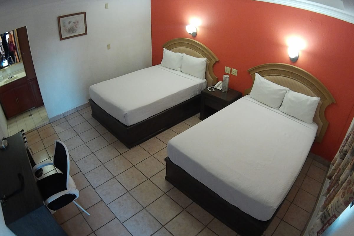 Una habitación de hotel con dos camas individuales, un escritorio con silla y una mesita con teléfono.