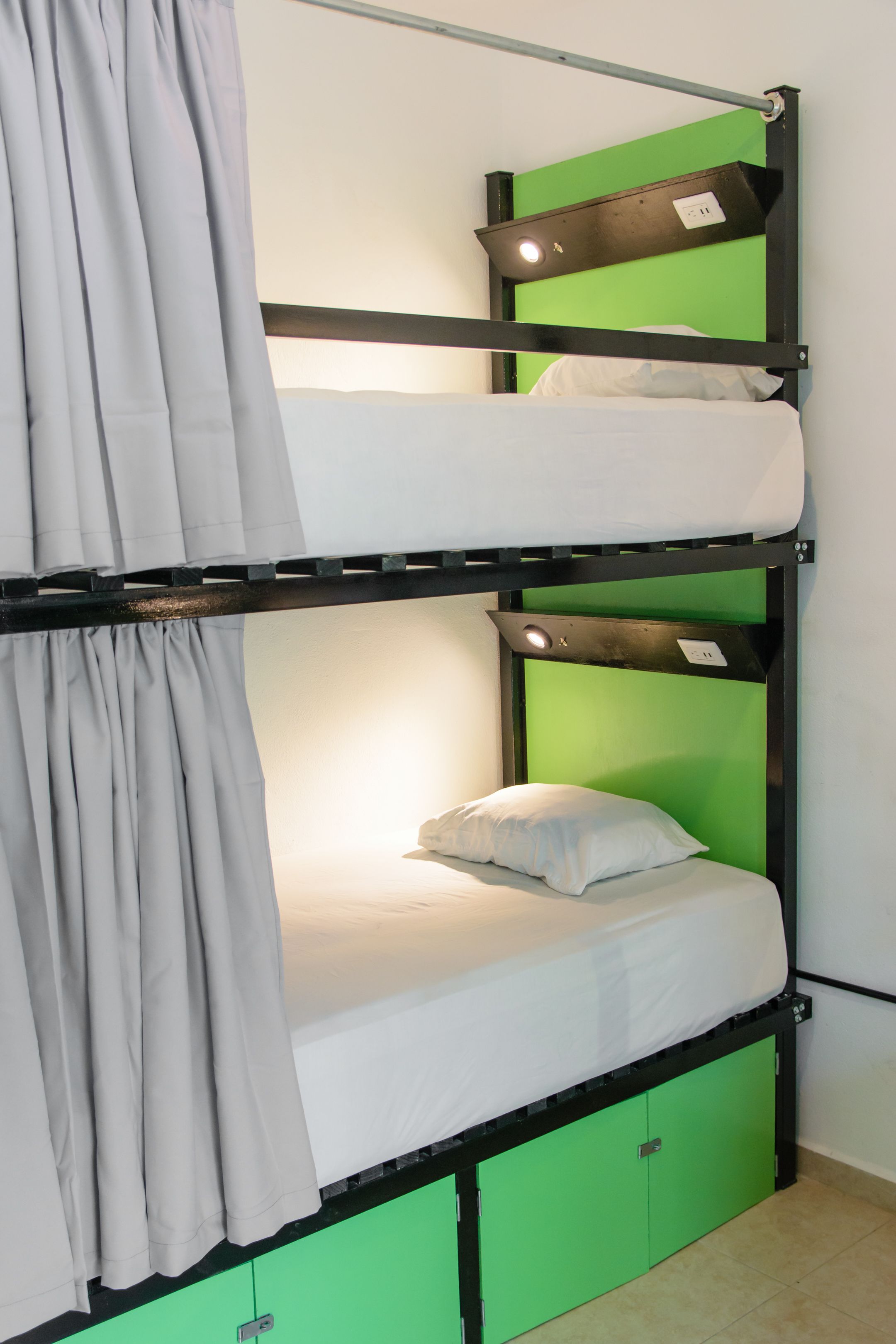Un lit superposé avec une tête de lit verte, un matelas blanc et un rideau gris.