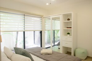 A modern bedroom with a bed, a bedside table, a wardrobe, and a window with blinds.