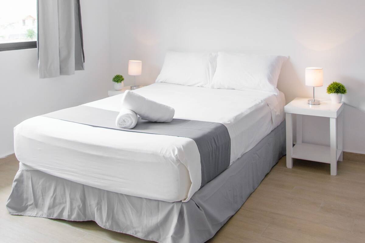 Ein modernes Schlafzimmer mit Bett, Deckenventilator, Nachttischlampen und einem Fenster mit Vorhängen.
