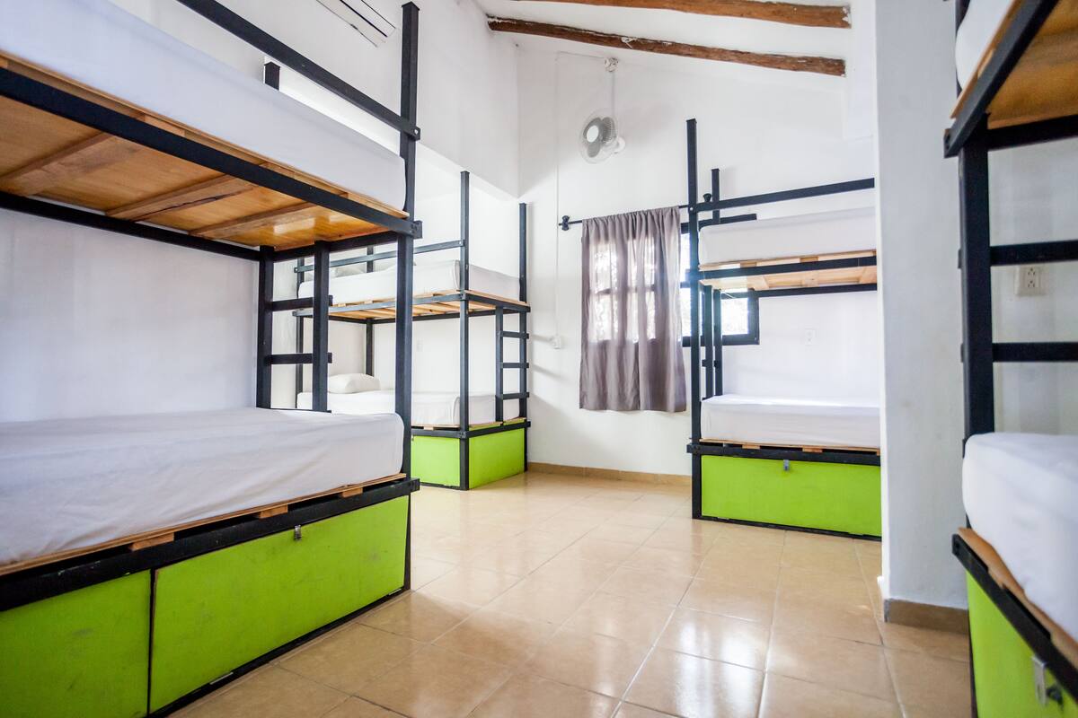 Ein Schlafsaalzimmer mit Etagenbetten, grünen Stauraumfächern und einem Deckenventilator.