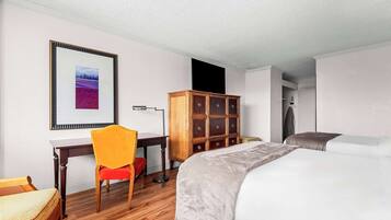 A hotel room with a bed, a desk, a chair, a wardrobe, and a framed picture on the wall.