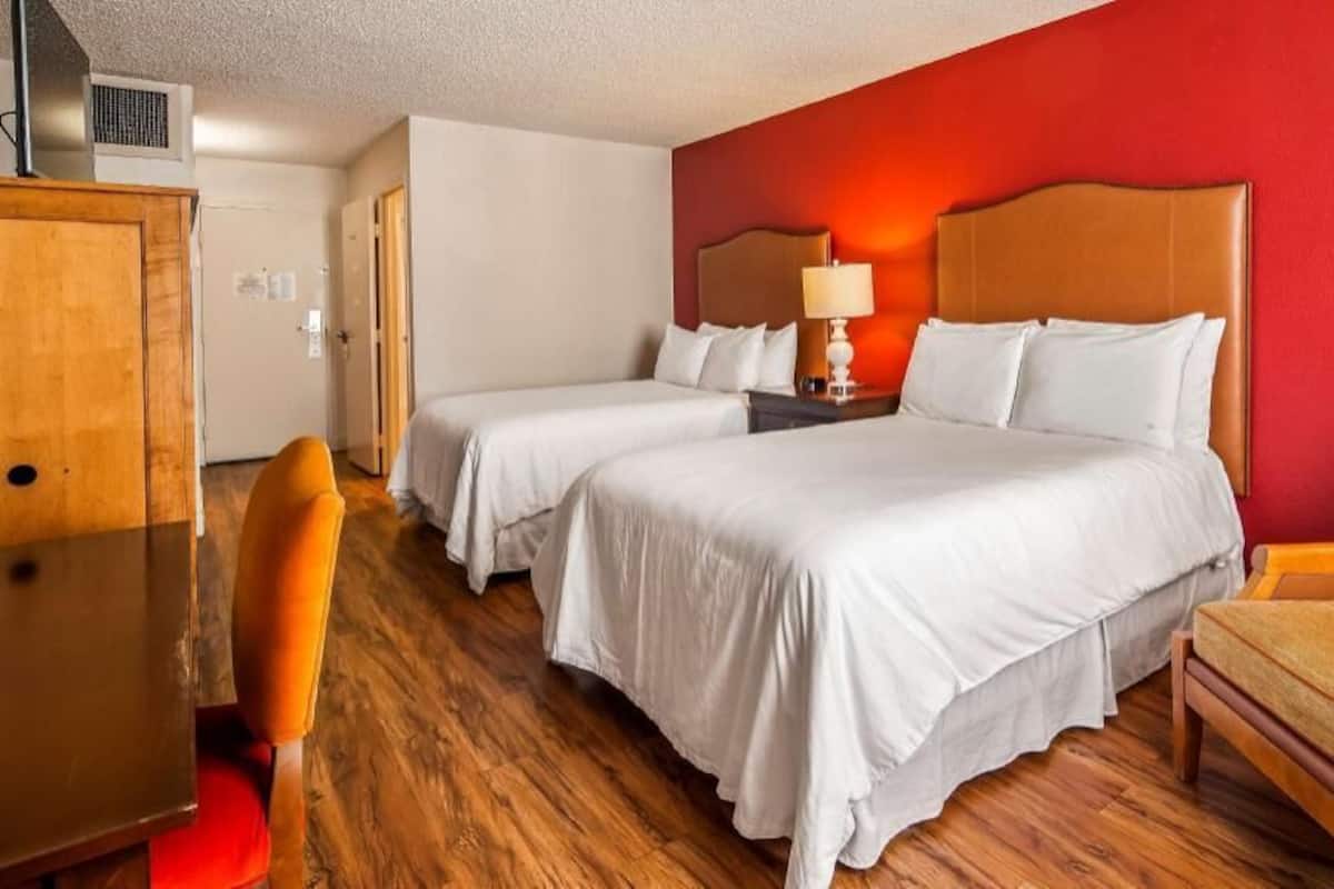 Habitación de hotel con dos camas, un escritorio de madera, una silla y una pared decorada en rojo.