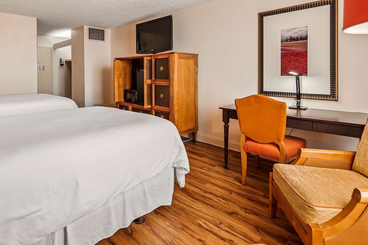 Habitación de hotel con dos camas, un escritorio con silla, televisor y un cuadro en la pared.