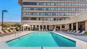 A swimming pool with lounge chairs and a building with multiple floors and large windows.