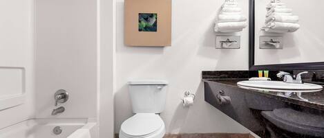 A modern bathroom with a bathtub, toilet, and vanity with a sink and mirror.