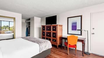 Una habitación de hotel con cama, escritorio, silla, armario y un cuadro enmarcado en la pared.