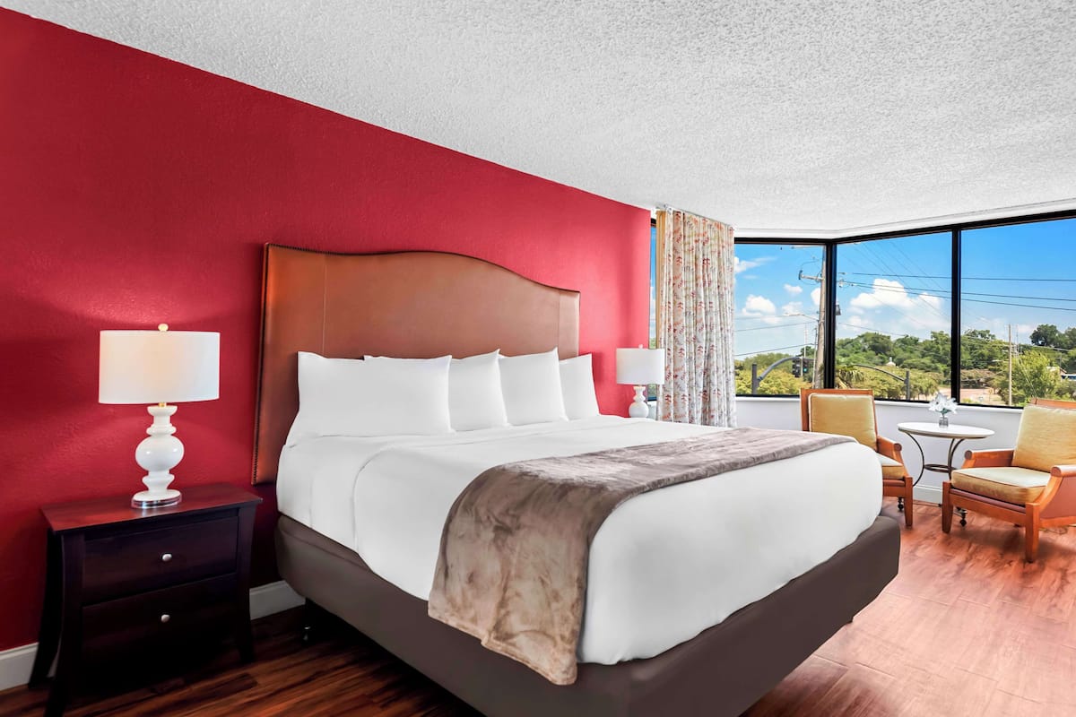 Habitación de hotel con una cama grande, una mesita de noche, dos sillas, una pequeña mesa y vistas al exterior.