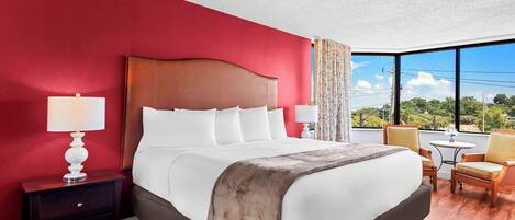 A hotel room with a large bed, a nightstand, two chairs, a small table, and a view of the outdoors.