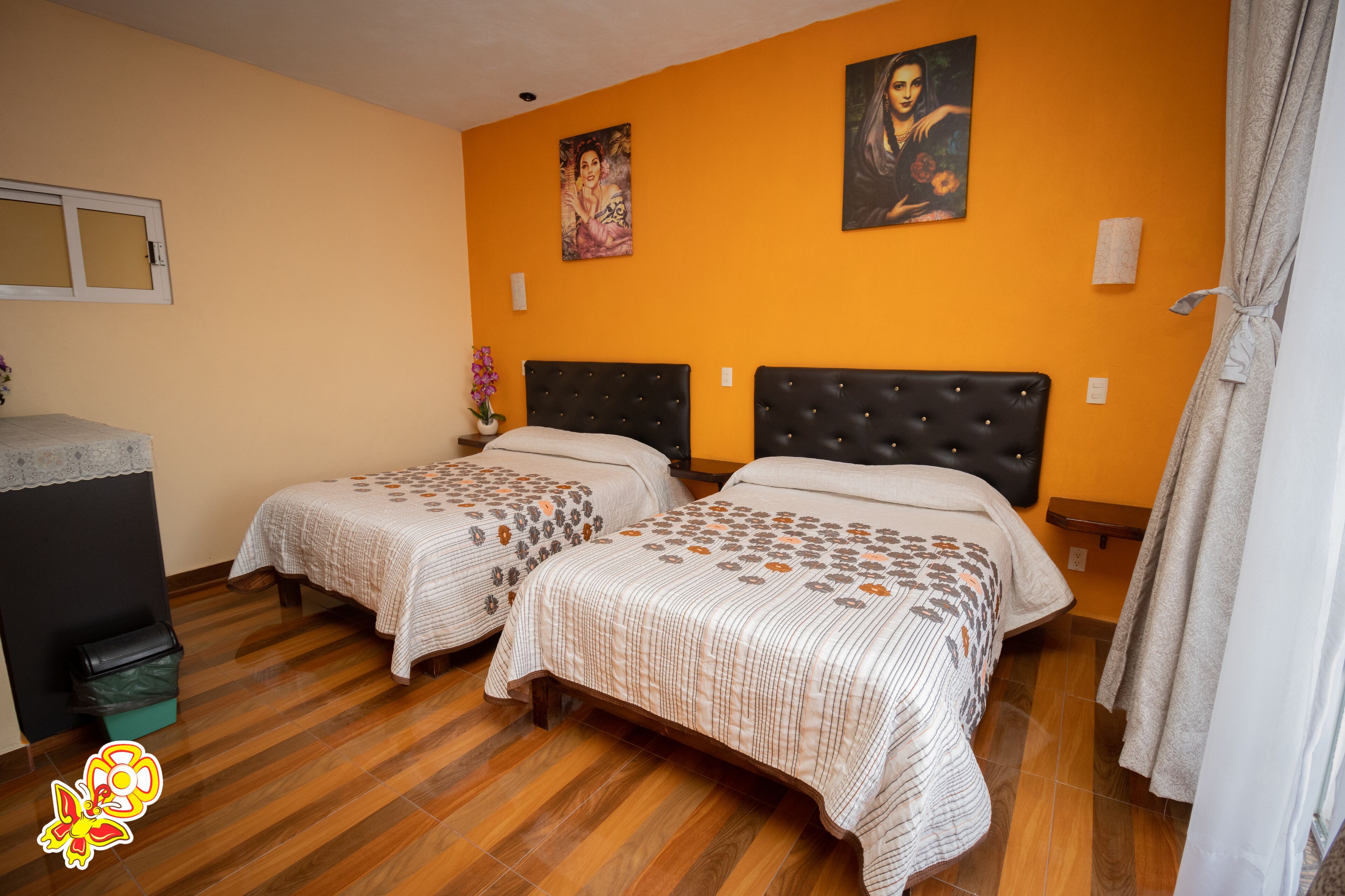 A hotel room with two beds, wooden flooring, and orange walls.