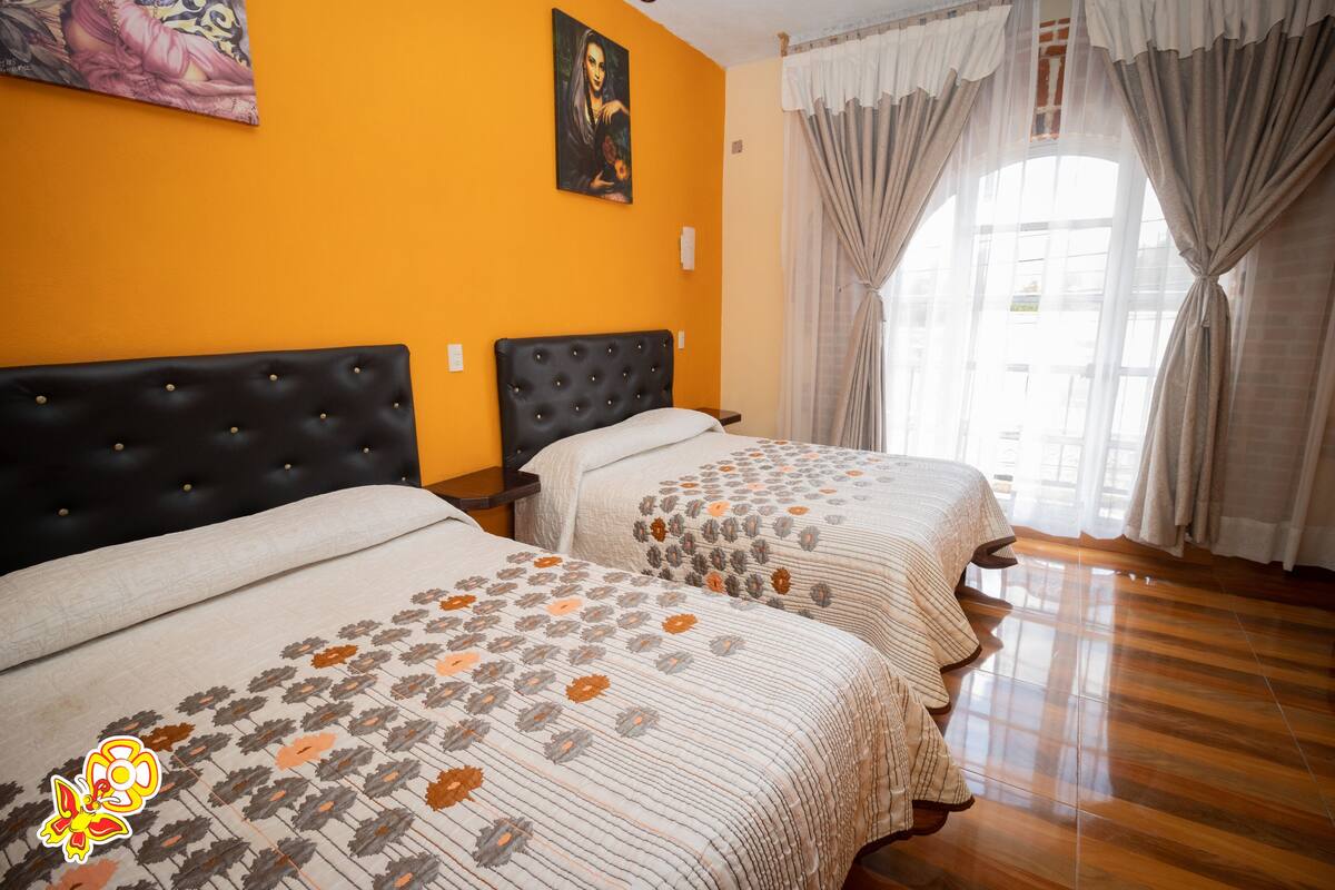 Une chambre d’hôtel avec deux lits, une grande fenêtre avec des rideaux et un tableau au mur.
