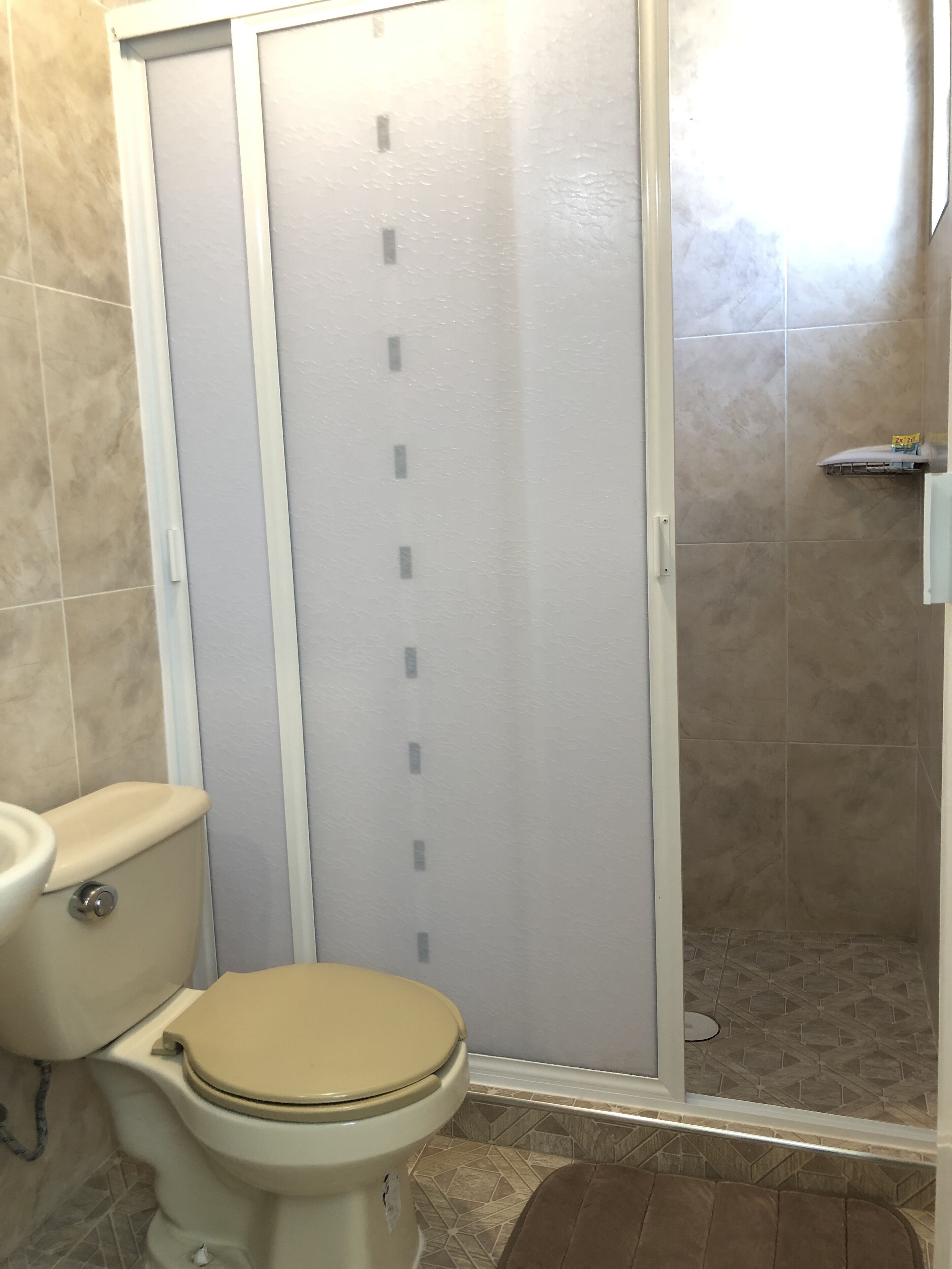 A bathroom with a toilet, a shower enclosure, and a tiled floor.