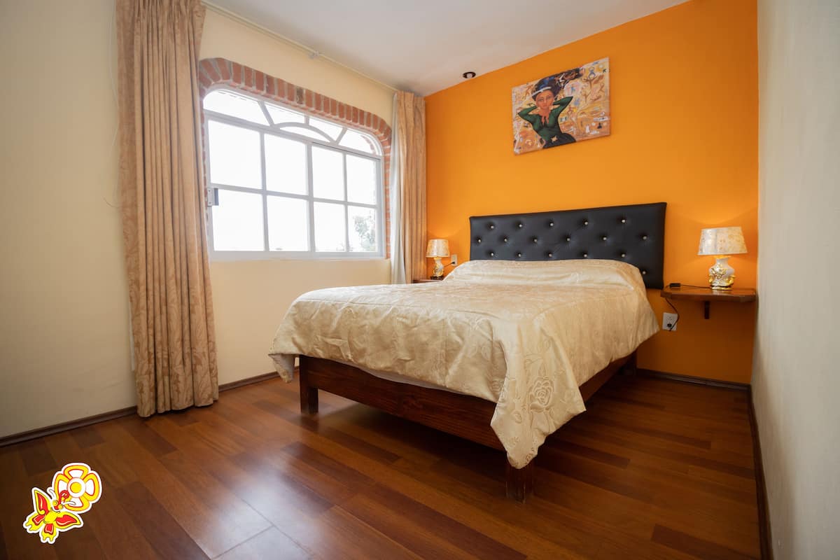 Une chambre avec un grand lit, une fenêtre avec des rideaux, un tableau au mur et deux lampes de chevet.