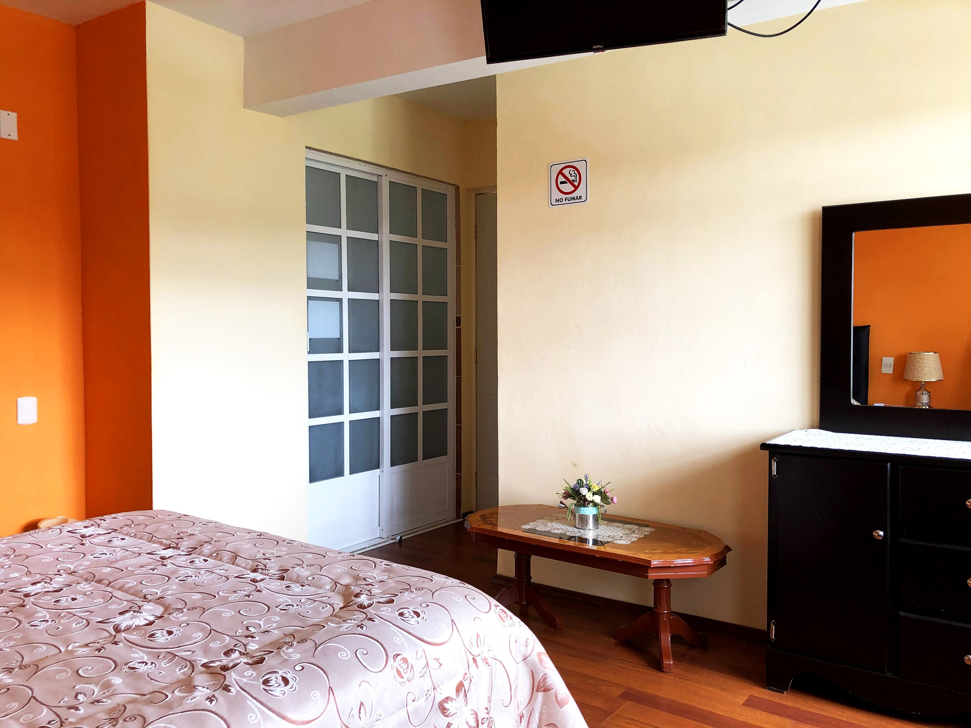 A bedroom with a bed, a dresser, a small table with a vase, a mirror, and a sliding door.