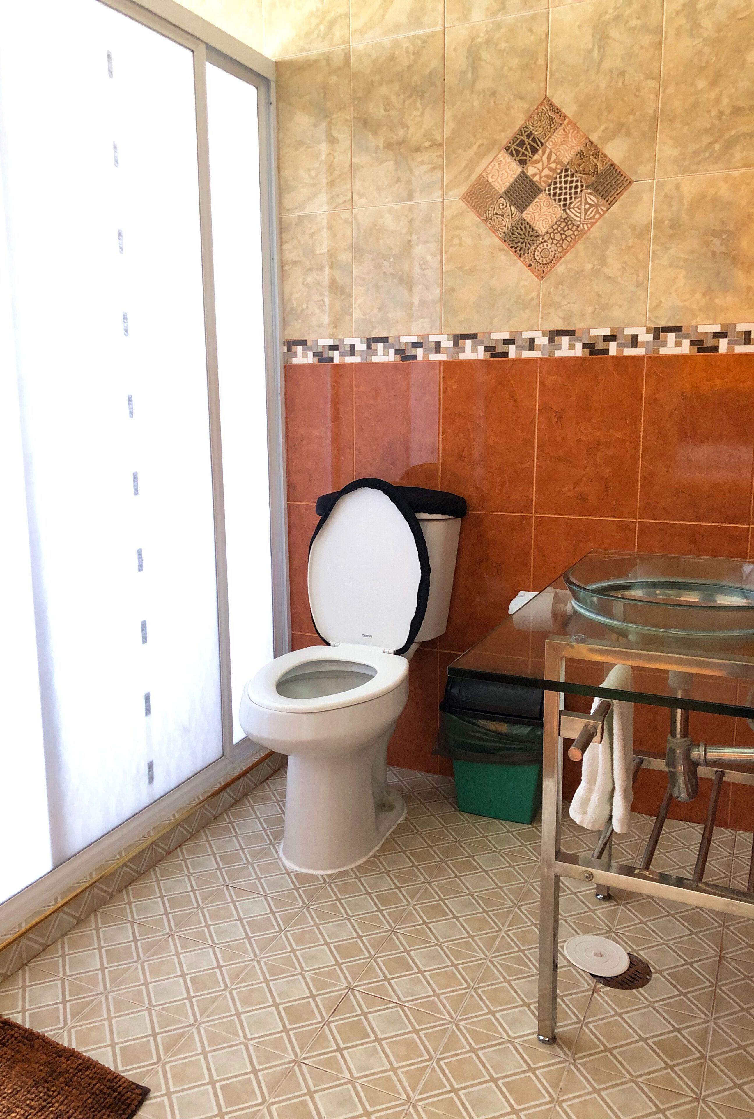 Een badkamer met een toilet, een glazen wastafel en een betegelde vloer.