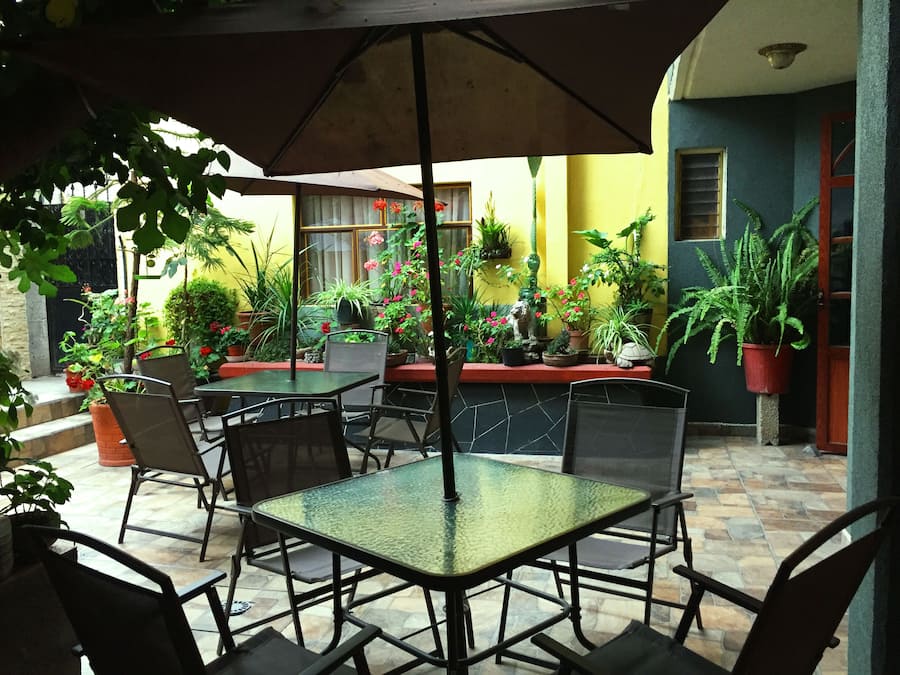 Un espace extérieur aménagé en terrasse, avec des tables et des chaises, entouré de plantes et de fleurs en pot.