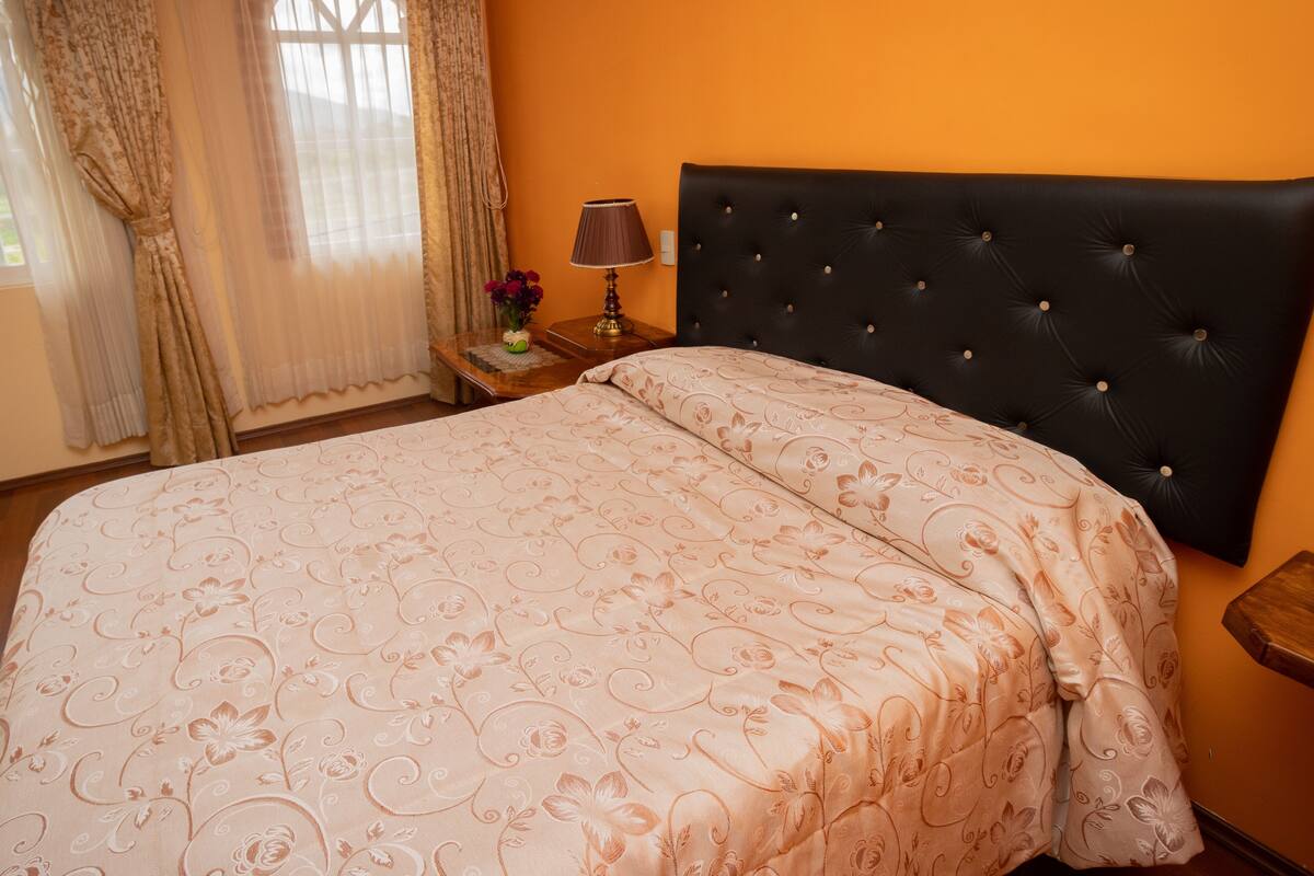 Une chambre à coucher avec un grand lit, une table de chevet avec une lampe et une fenêtre avec des rideaux.