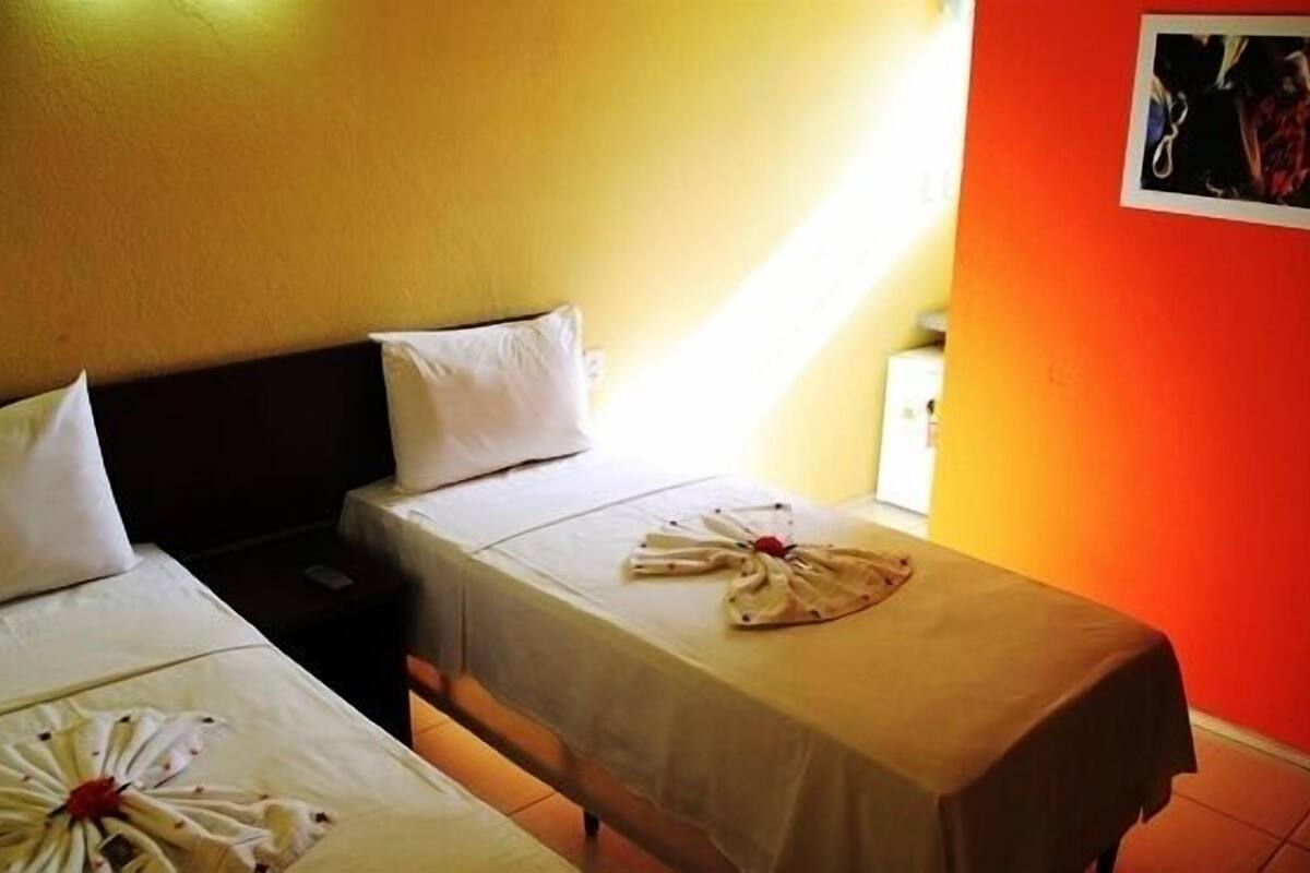 Habitación de hotel con dos camas, cada una con sábanas blancas y una toalla dispuesta en forma de círculo.