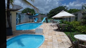 Piscina com escorregas, guarda-sol e mobiliário de exterior.