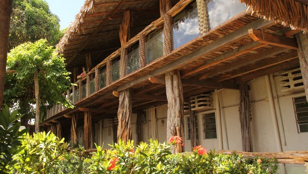 Uma estrutura de madeira tradicional com telhado de palha, várias varandas e um jardim florido.