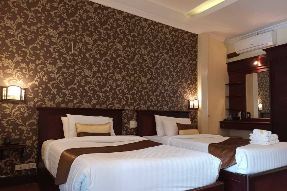 A hotel room with two beds, a large mirror, and a wall with a floral pattern.
