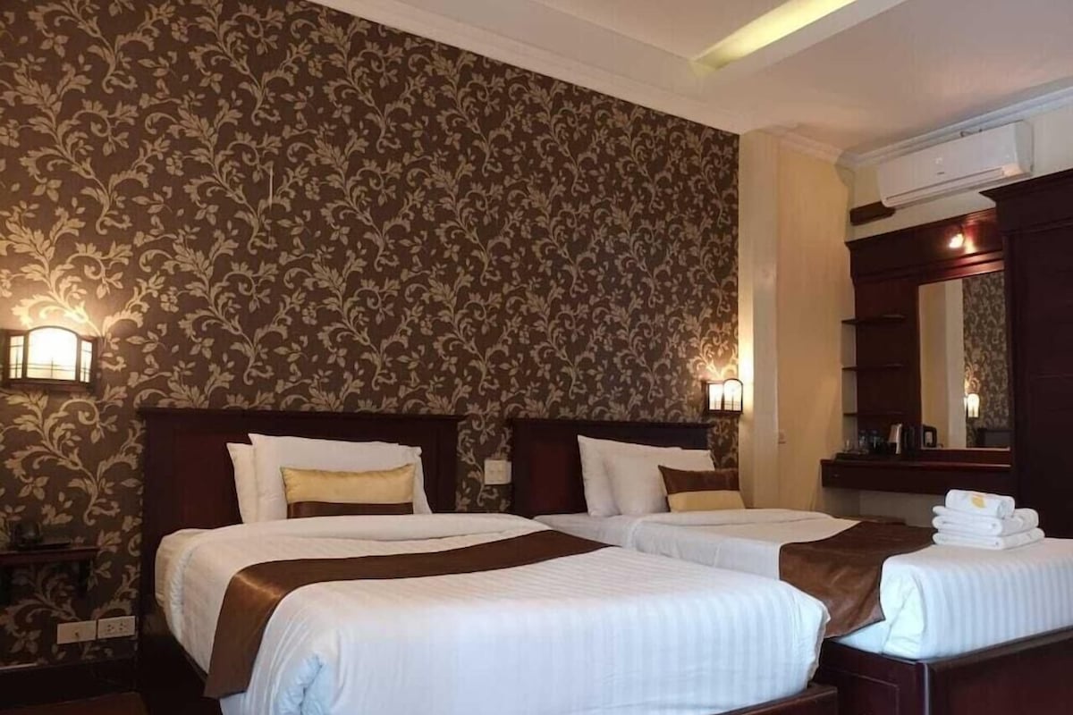 Une chambre d’hôtel avec deux lits, un grand miroir et un mur orné d’un motif floral.