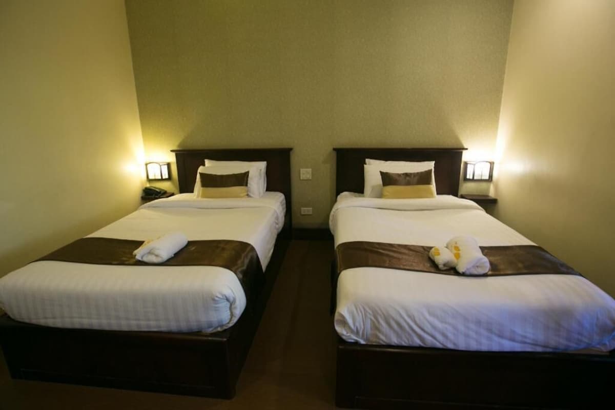 Deux lits jumeaux avec du linge de lit blanc et des têtes de lit marron, chacun étant muni d’une lampe de chevet et d’une serviette pliée posée sur le lit.