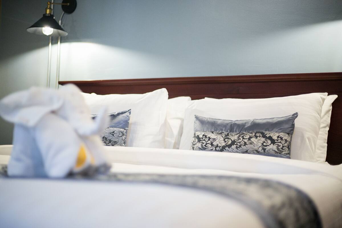 A neatly made bed with white and patterned pillows, a wooden headboard, and a hanging lamp.