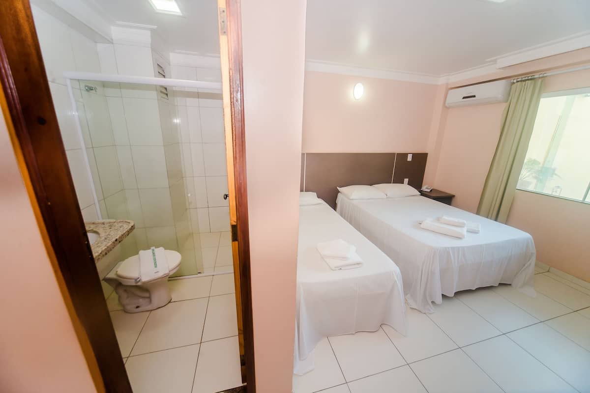 Habitación de hotel con ducha, inodoro, dos camas y una mesita de noche.