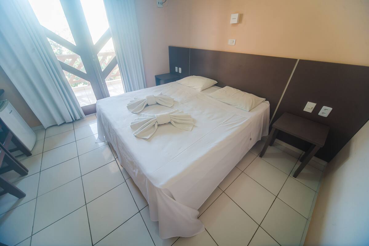 Habitación de hotel con cama, mesita de noche, una silla y vistas al exterior.