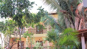 A multi-story building with balconies, surrounded by lush tropical vegetation including palm trees and various shrubs. - Pousada d'Areia (Barreirinhas)