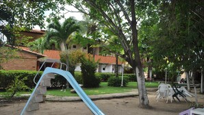 Um parquinho com um escorrega azul, rodeado por árvores e um edifício com telhado vermelho.