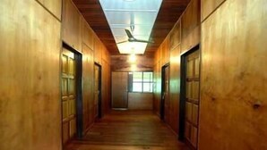 Un couloir en bois, avec des portes de chaque côté, un ventilateur de plafond et une fenêtre au bout.