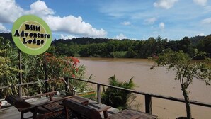 Une terrasse dotée de meubles en bois, donnant sur une rivière et entourée d’une végétation luxuriante.