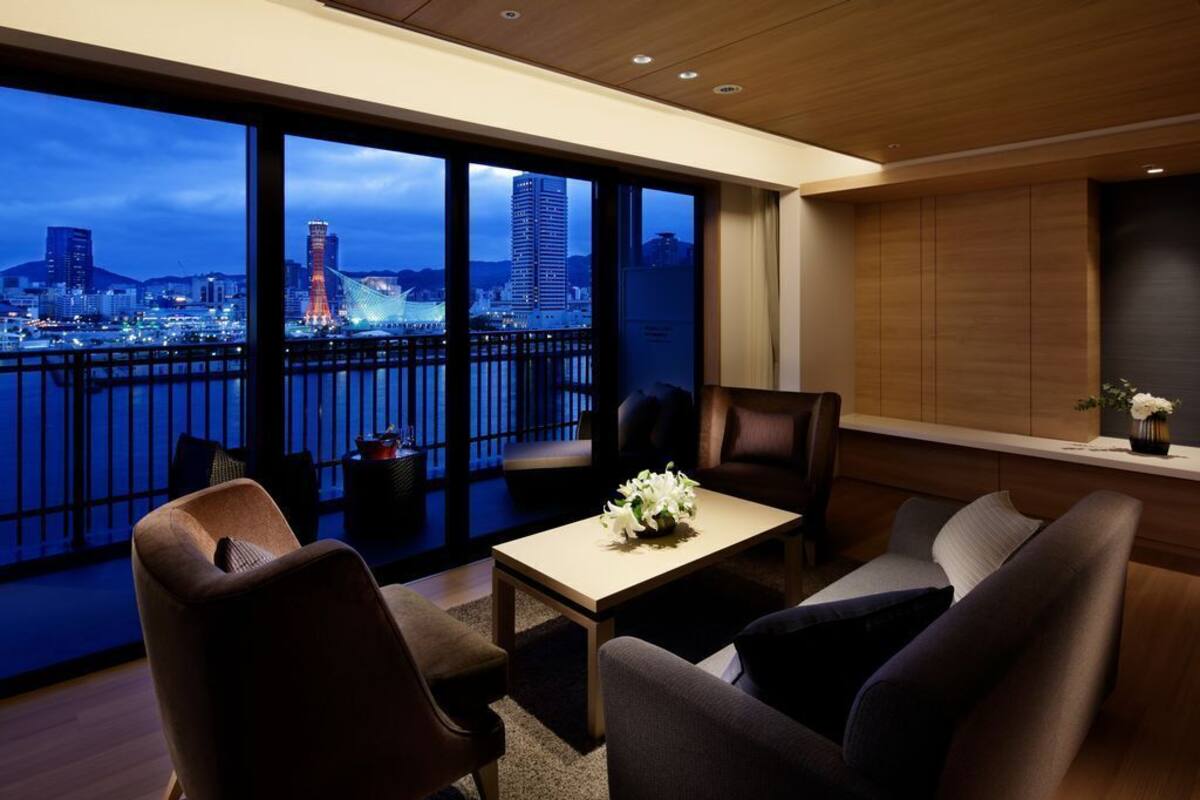 Een moderne hotelkamer met balkon, grote ramen, een bank, een tafel en uitzicht op de stadsgezicht.