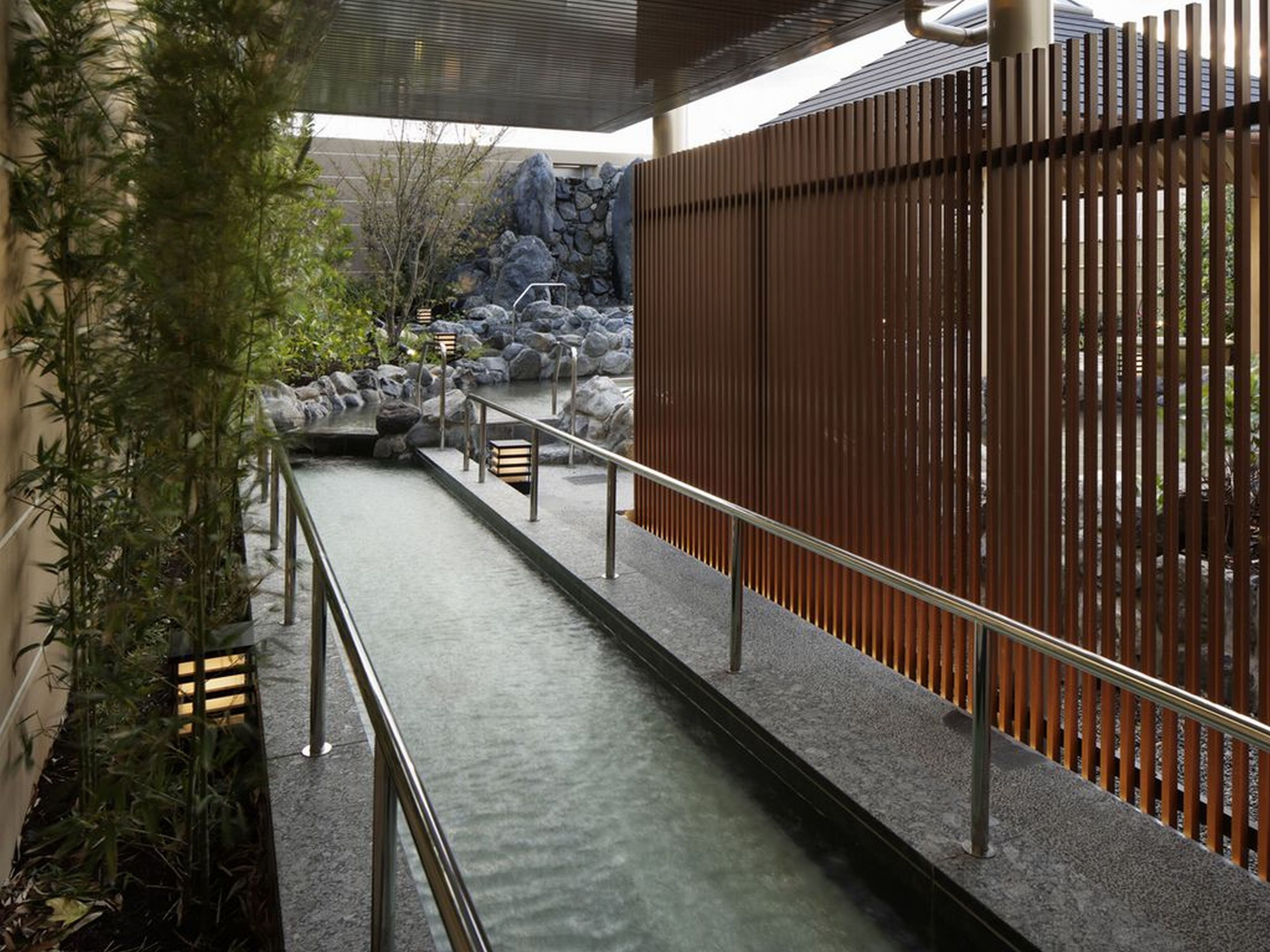 A corridor with a water feature, bamboo plants, and a stone wall.