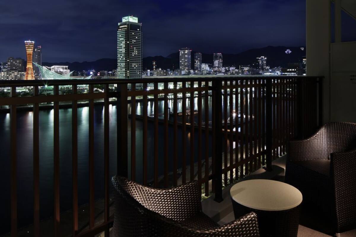 Een balkon met rieten meubilair, uitzicht op een stadshemel en een wateroppervlak.