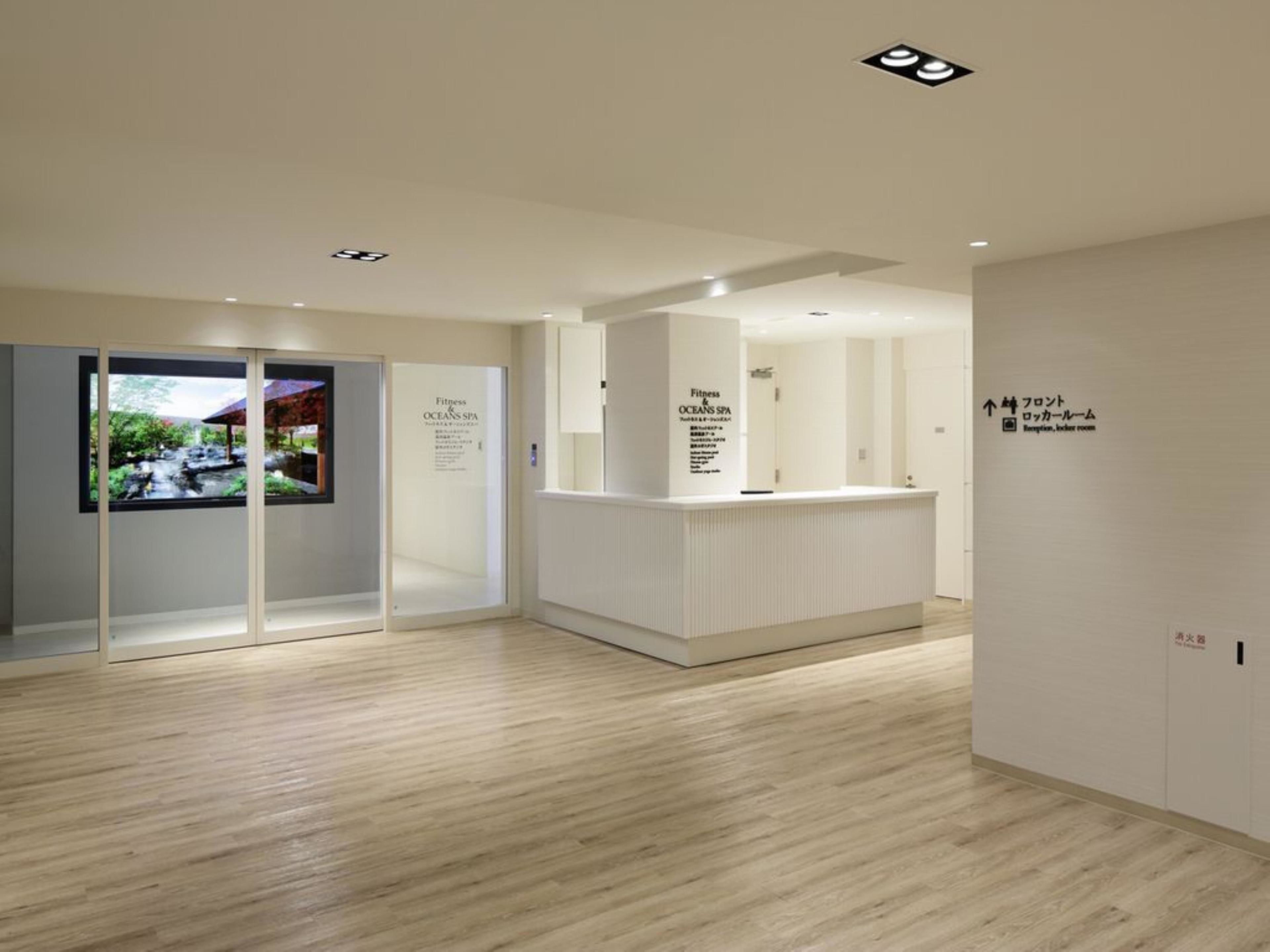A reception area with a reception desk, glass doors leading to a waiting area, and a sign indicating the location of the reception and locker room.