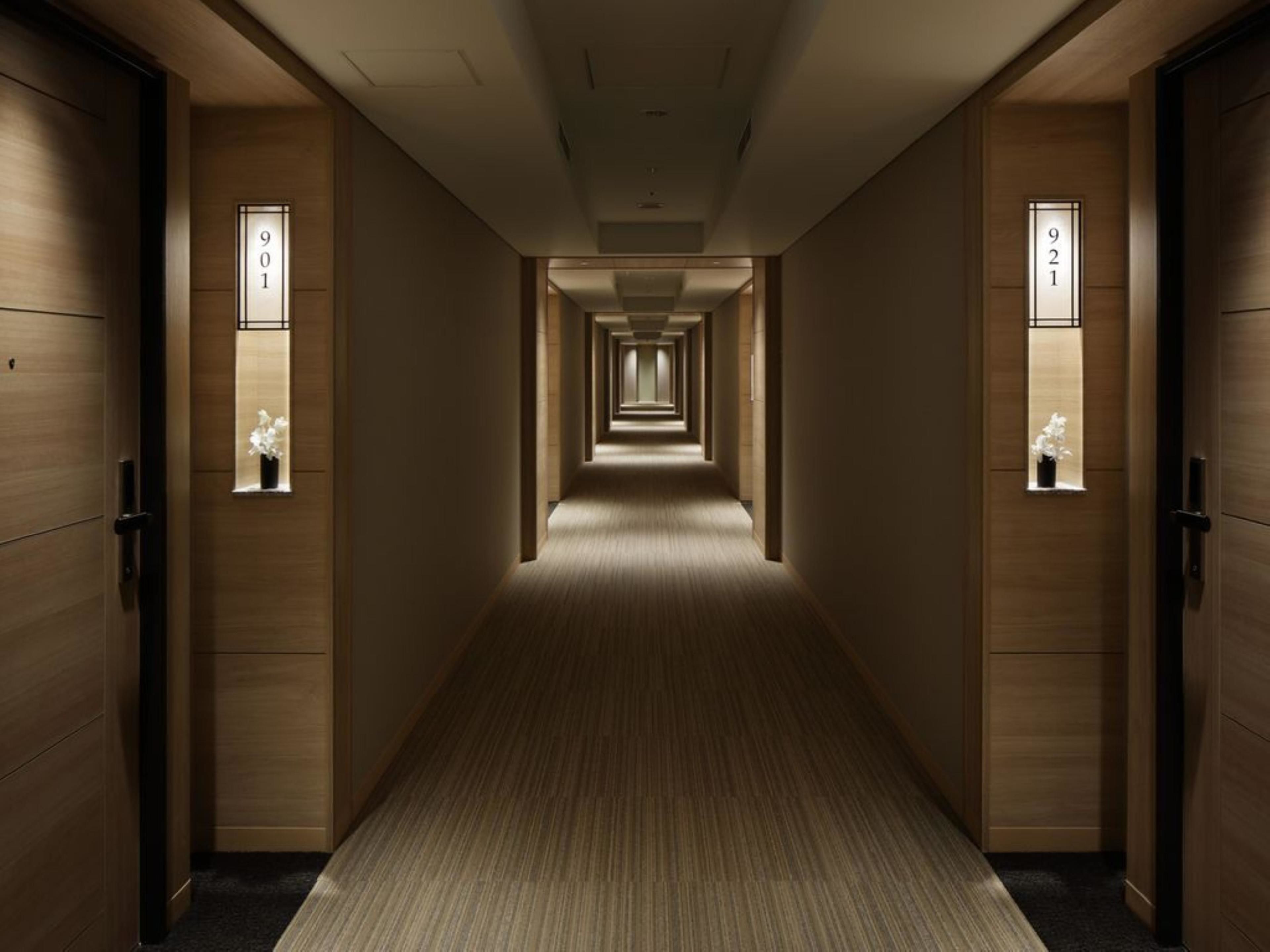 A hotel corridor with wooden walls, numbered doors, and small windows with flowers.