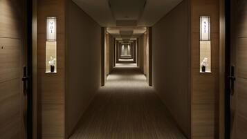 A hotel corridor with wooden walls, numbered doors, and small windows with flowers.