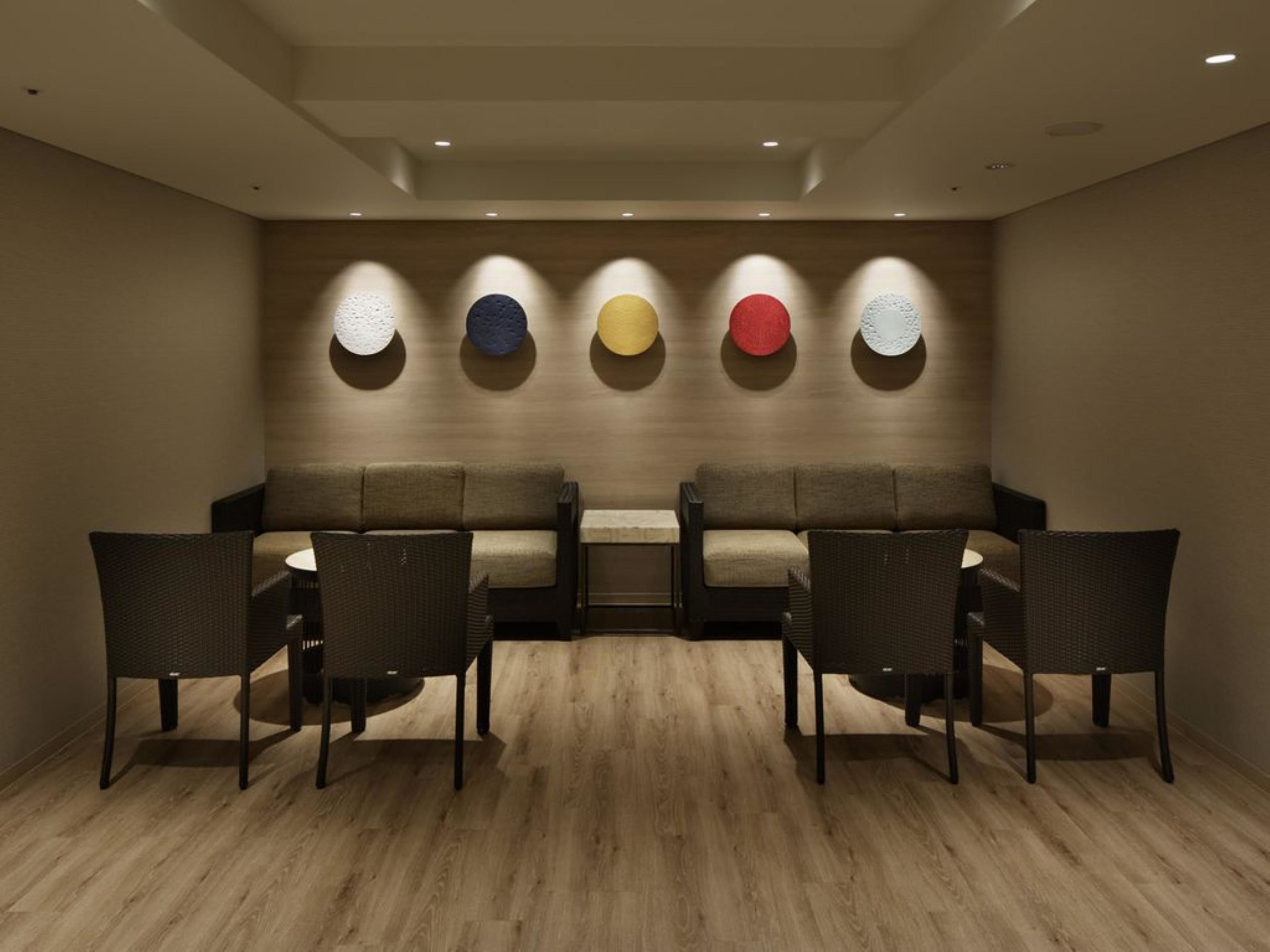 A modern lounge with a sofa and chairs, wooden flooring, and wall-mounted lighting.