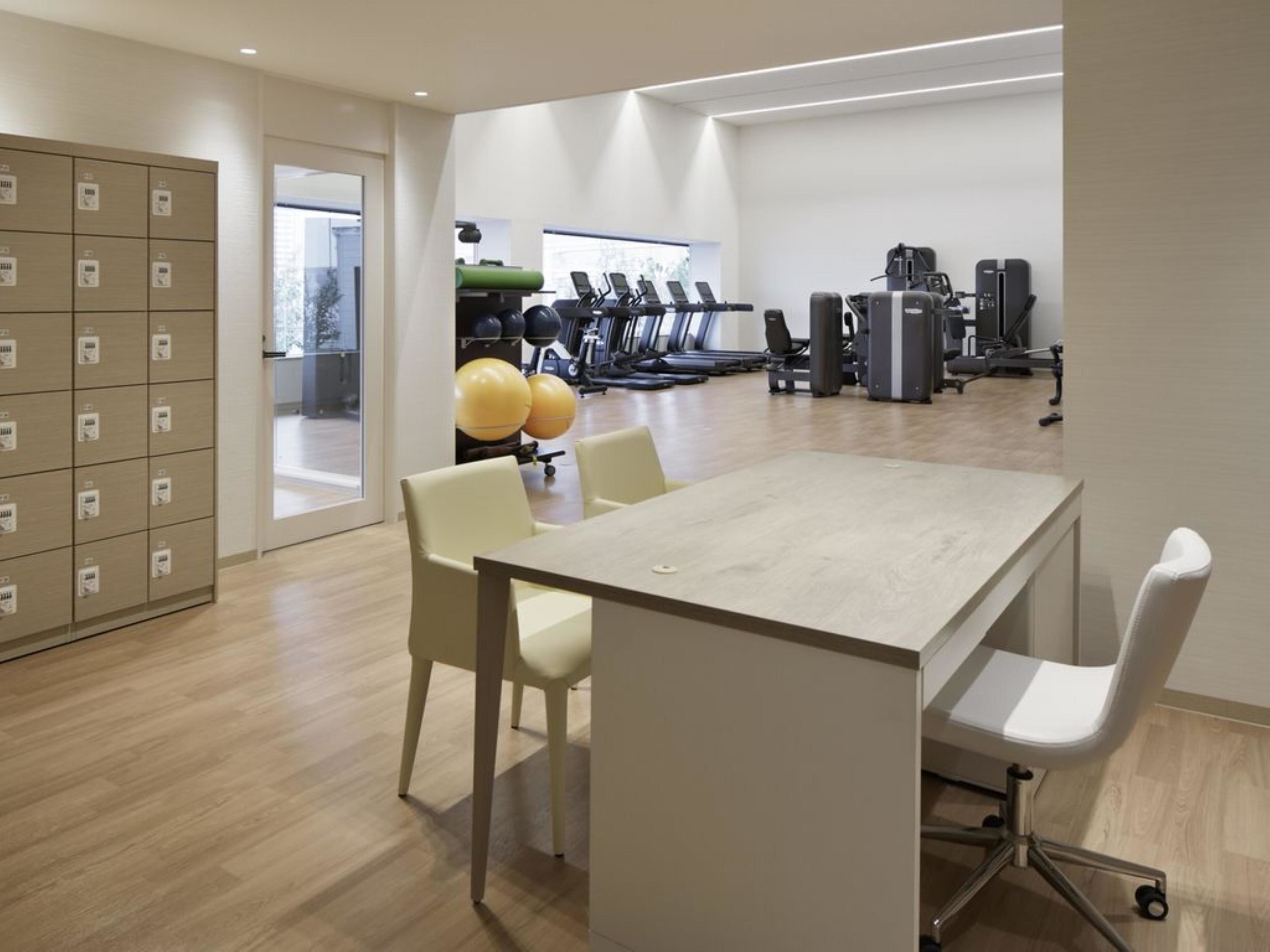 A modern gym with exercise equipment, a large table, and lockers.