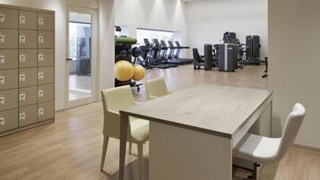 A modern gym with exercise equipment, a large table, and lockers.