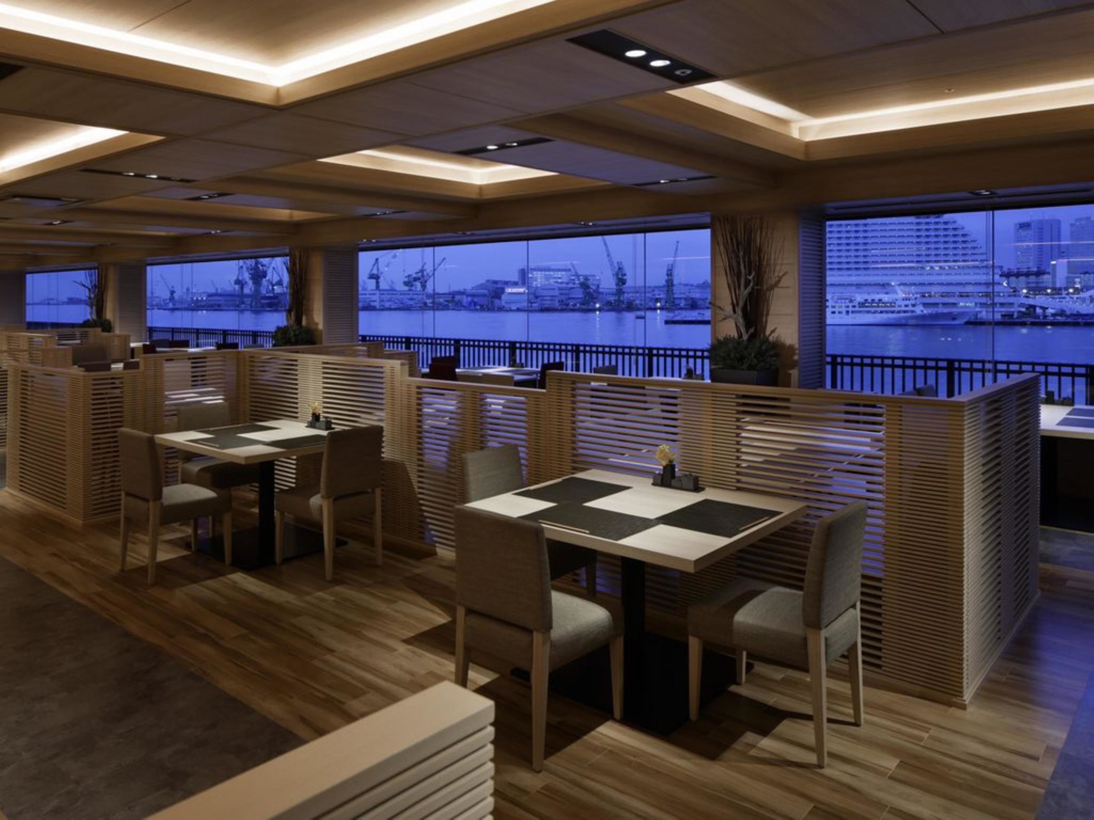 A modern restaurant with wooden furniture and large windows overlooking a waterfront.