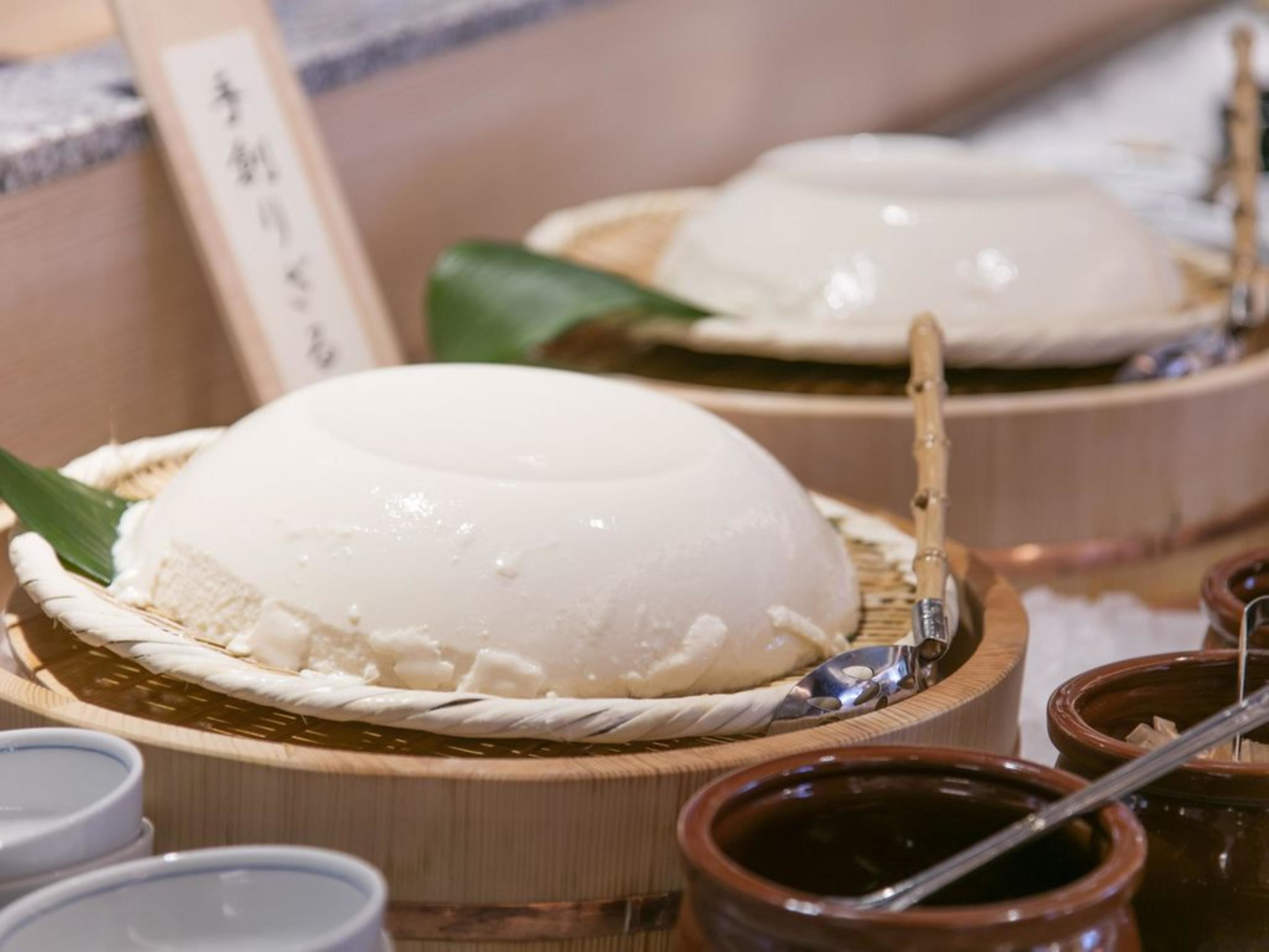A traditional Japanese meal setup with a white, dome-shaped dish on a woven mat, accompanied by small bowls and a bamboo spoon.