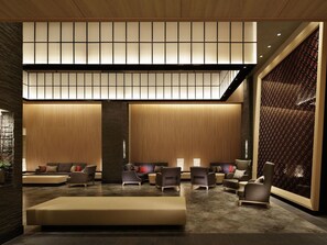 En moderne lobby med højt til loftet, indbygget belysning og et siddeområde med sofaer og lænestole.