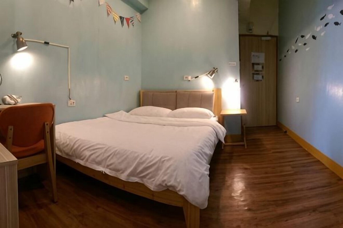 A bedroom with a bed, bedside lamps, a chair, and a wooden floor.